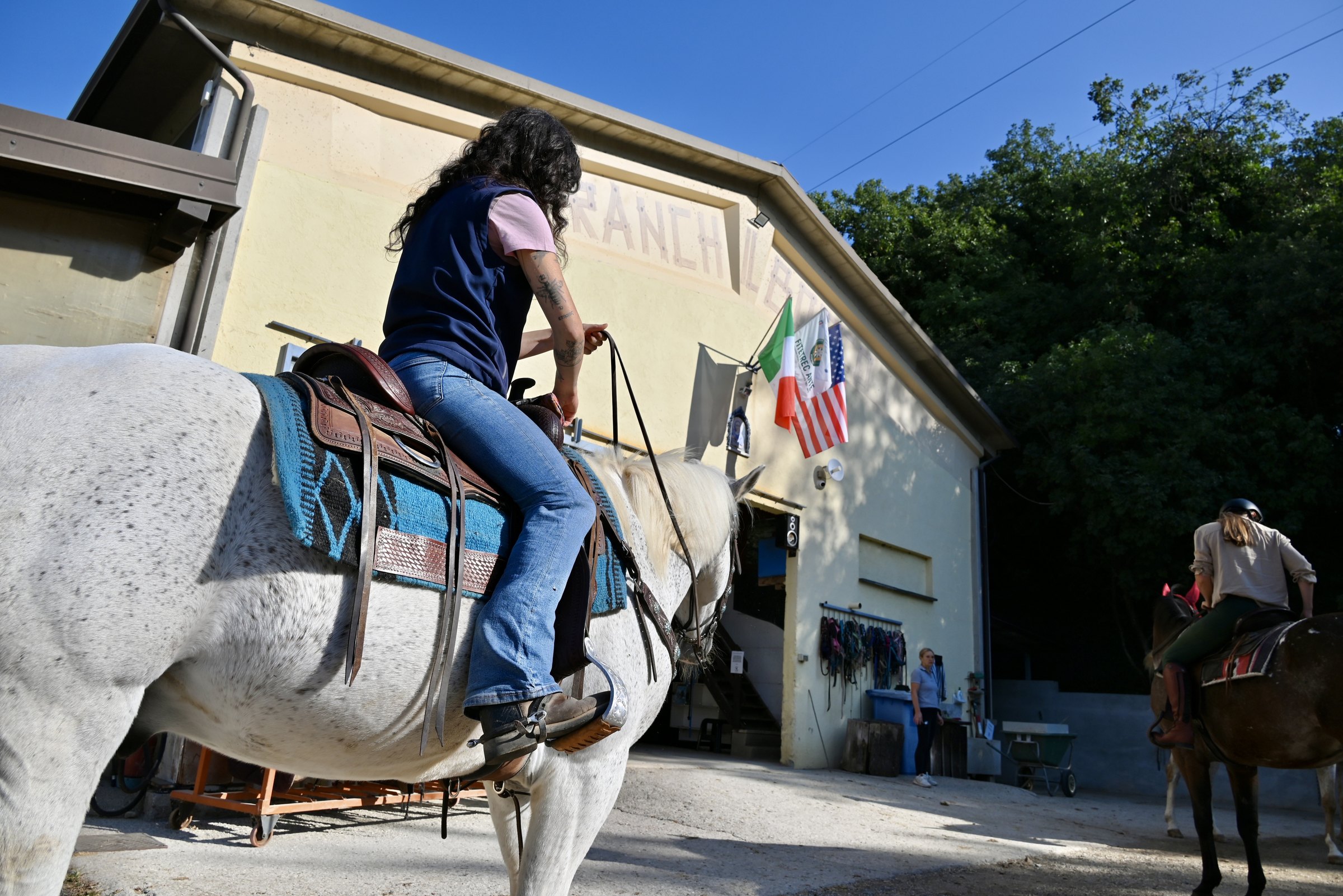 Una cavallerizza su un cavallo bianco davanti alle scuderie